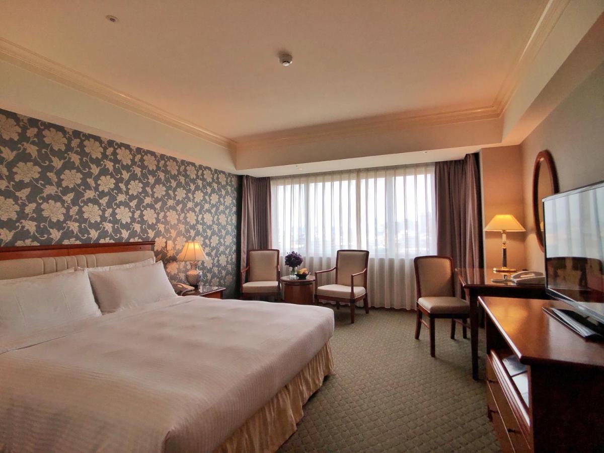 Evergreen Laurel Hotel - Taichung Exterior foto The photo shows a well-appointed hotel room. It features a large bed with white bedding and a decorative headboard. The walls are adorned with a patterned wallpaper, possibly floral, adding a touch of elegance. There is a window with sheer curtains t