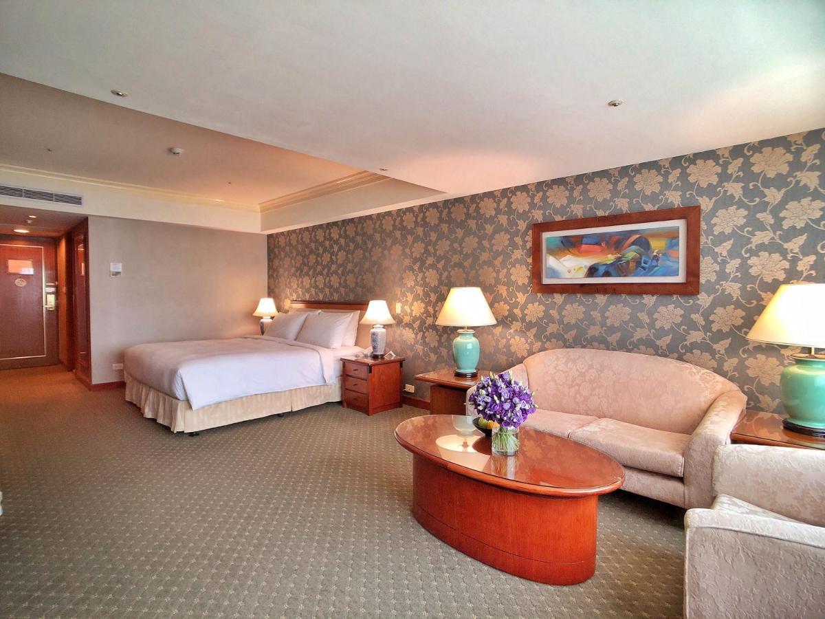 Evergreen Laurel Hotel - Taichung Exterior foto The photo shows a hotel room that features a well-furnished space. It includes a large bed with a light-colored bedspread, a comfortable sofa, and armchair. There's a coffee table with a vase of flowers in the center. The room has a decorative wallpa