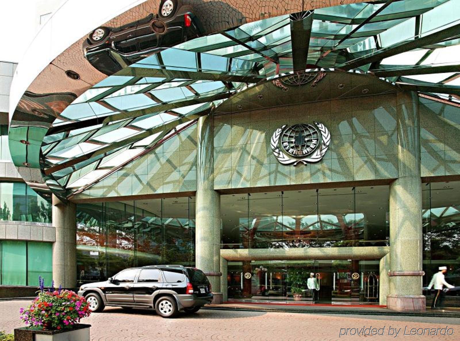 Evergreen Laurel Hotel - Taichung Exterior foto The photo shows the entrance of a modern building characterized by its glass and metal architecture. The structure features a large, domed roof that reflects light, with a distinctive emblem or logo displayed prominently at the center. In front of th