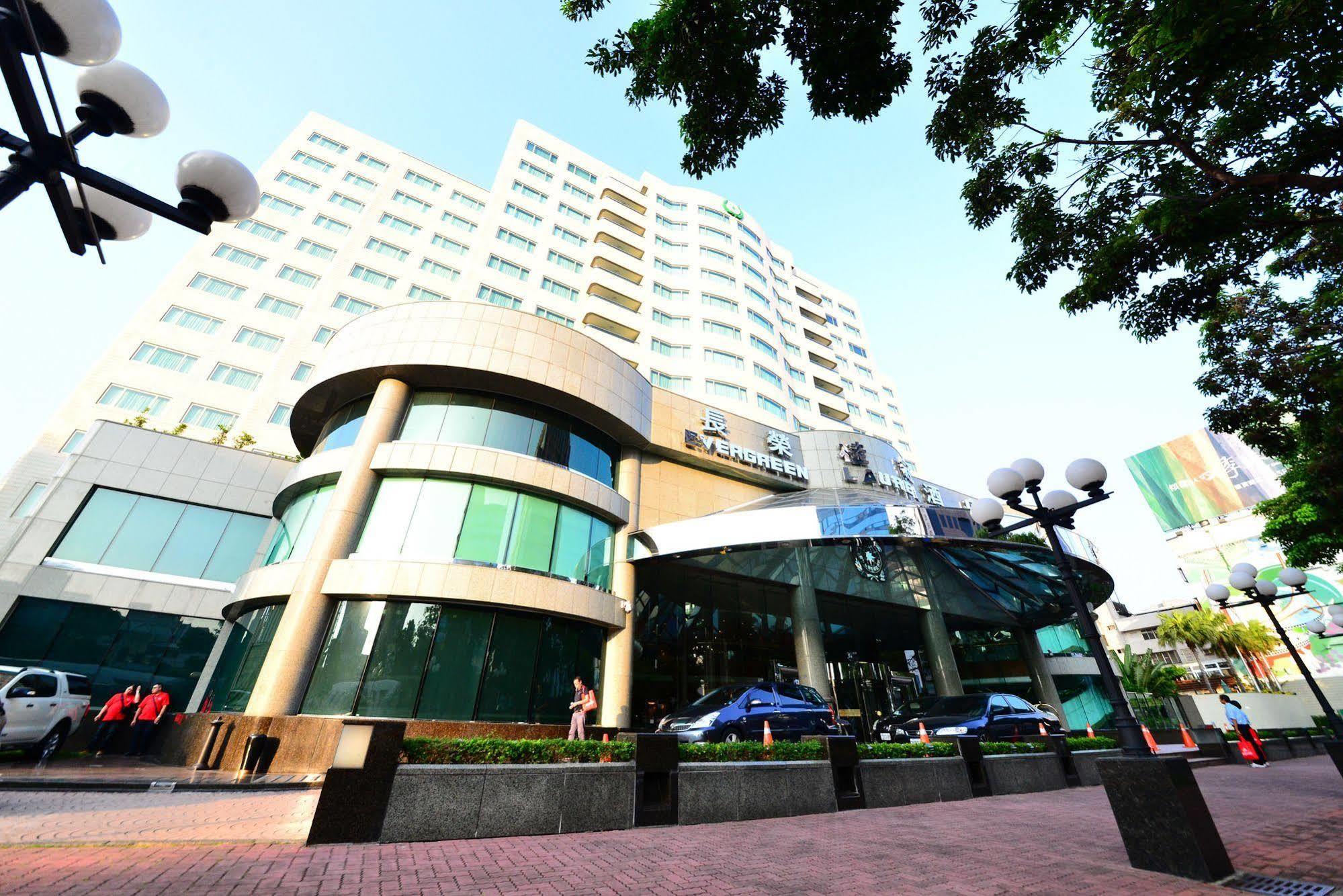 Evergreen Laurel Hotel - Taichung Exterior foto The photo shows a modern multi-story building, which appears to be a hotel or commercial establishment. The structure has a rounded glass entrance with a distinctive architectural design, featuring large windows. The building is surrounded by greener