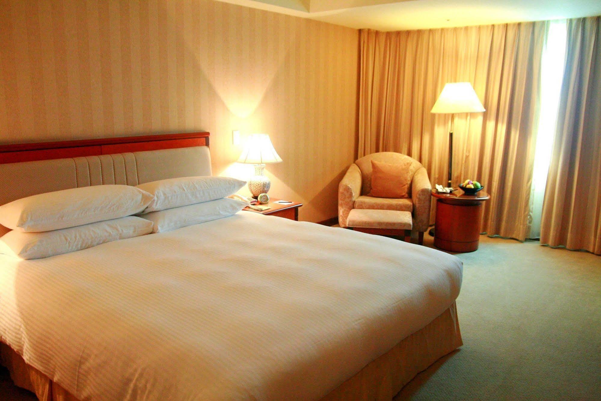 Evergreen Laurel Hotel - Taichung Exterior foto The photo shows a hotel room containing a large bed with white linens, flanked by two bedside lamps. To one side, there is a cozy armchair and a small side table with a fruit bowl or snacks. The walls are decorated in a soft, neutral color, and there
