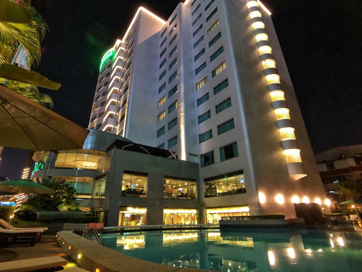 Evergreen Laurel Hotel - Taichung Exterior foto The photo shows a tall hotel building at night, illuminated by lights. The architecture appears modern, with several floors and large windows. In the foreground, there is a swimming pool that reflects the lights from the building, creating a serene a