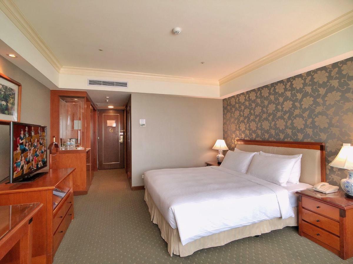Evergreen Laurel Hotel - Taichung Exterior foto The photo shows a well-furnished hotel room. It features a large bed with white linens positioned against a decorative wall. On either side of the bed are bedside tables with lamps. There’s a television mounted on a wooden cabinet across from the bed