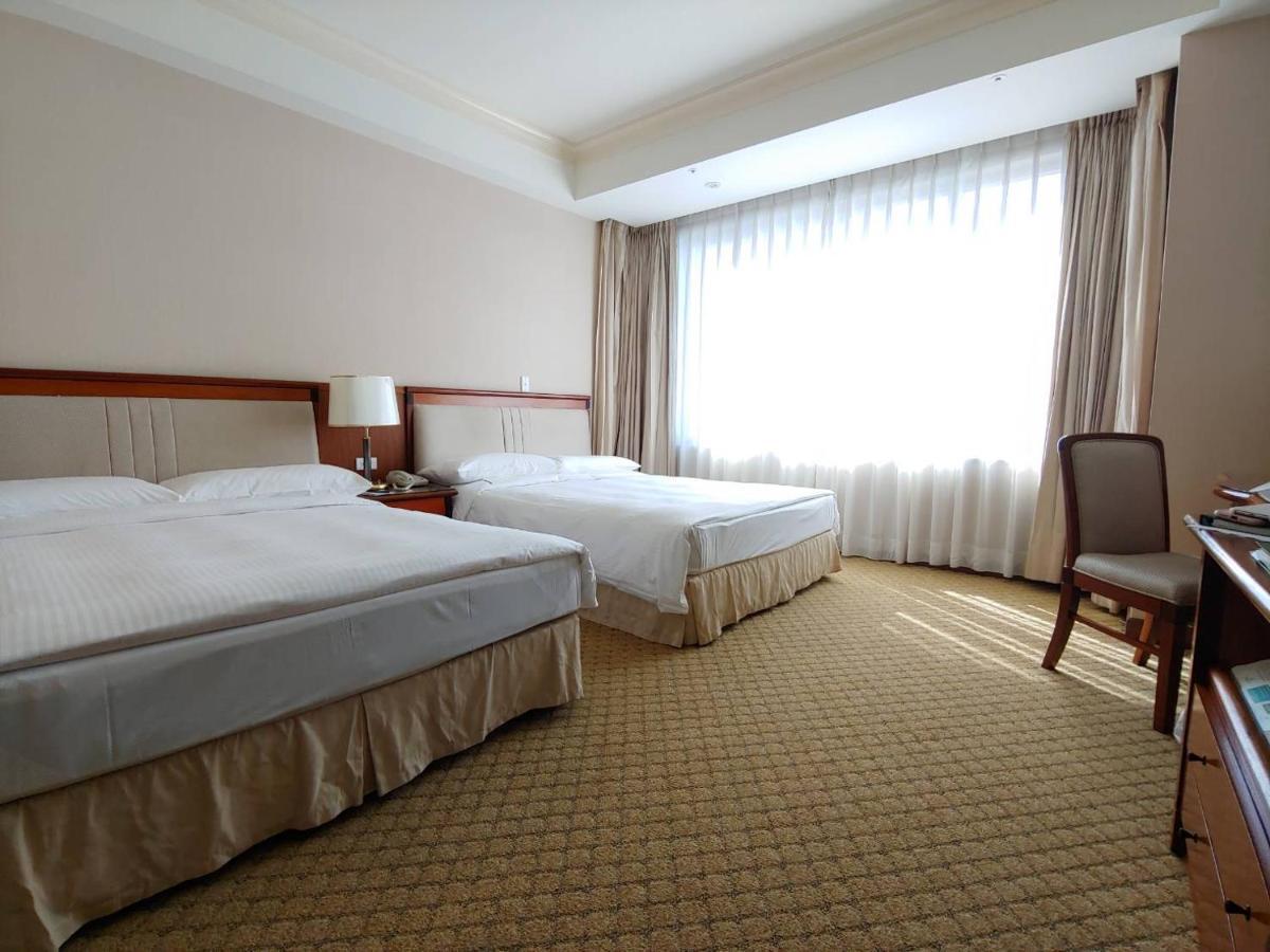 Evergreen Laurel Hotel - Taichung Exterior foto The photo shows a neatly arranged hotel room featuring two beds: one double bed and one single bed. The room has beige walls and a warm color palette. Large windows with sheer curtains allow natural light to flood in, creating a bright and airy atmos